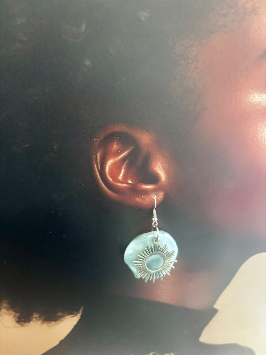 Boucle d'oreille à crochet avec soleil argenté sur pétale bleu nacré, portée à l'oreille
