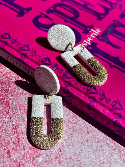 Boucles d’oreilles légères blanches et dorées de la marque Les Trésors de Cia, avec design élégant et sophistiqué.