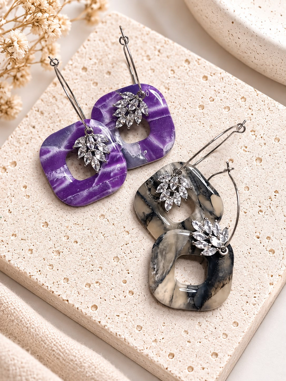 Deux paires de créoles carrées évidées en argile polymère, coloris violet marbré et noir et beige, ornées d'un bouquet de strass zirconium