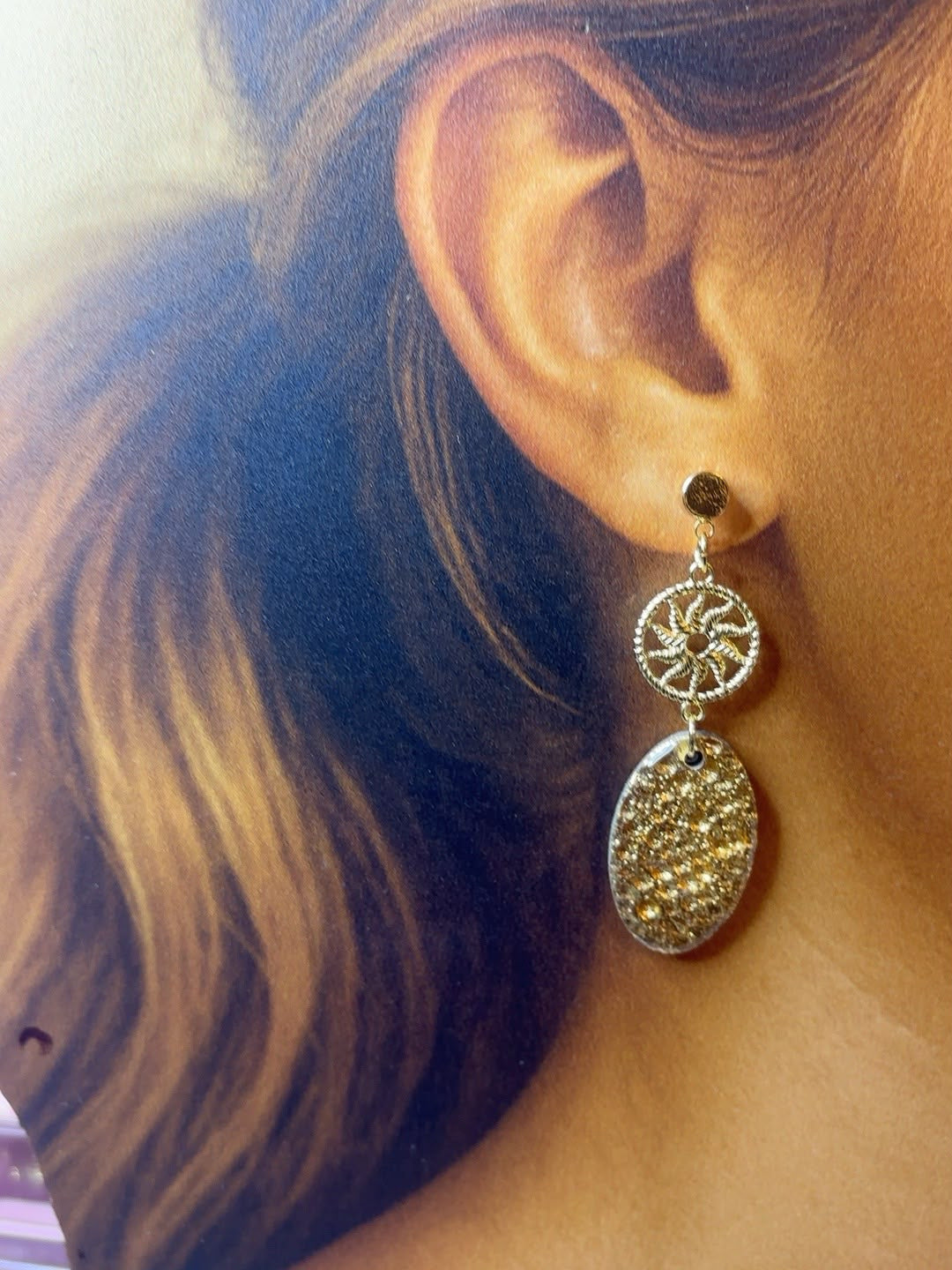 Boucle d'oreille pendante dorée portée à l'oreille : puce ronde, rosace ajourée et ovale doré pailleté effet or martelé