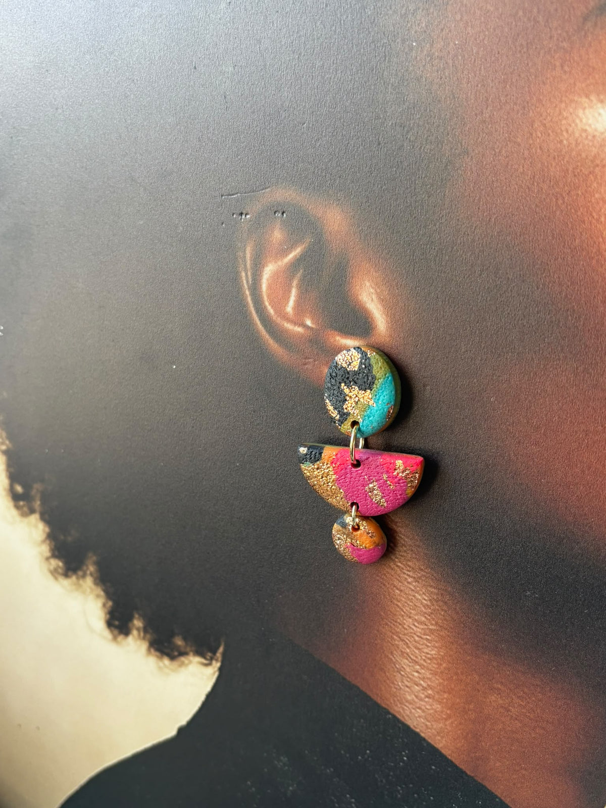 Boucle d'oreille portée : puce, demi-lune et petit disque en argile fuchsia, turquoise et noire à la feuille dorée
