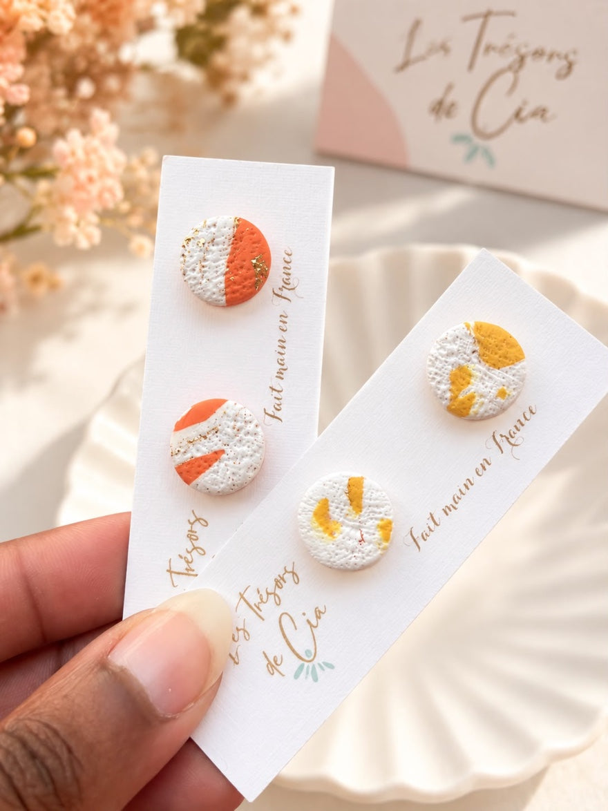 Puces d'oreilles rondes en argile polymère blanche texturée, l'une avec un aplat orange, l'autre avec des éclats jaunes