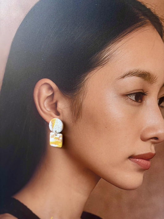 Boucles d'oreilles en argile polymère blanc texturé et jaune soleil, puce ronde surmontant un carré aux angles arrondis, la couleur traverse la surface en diagonale