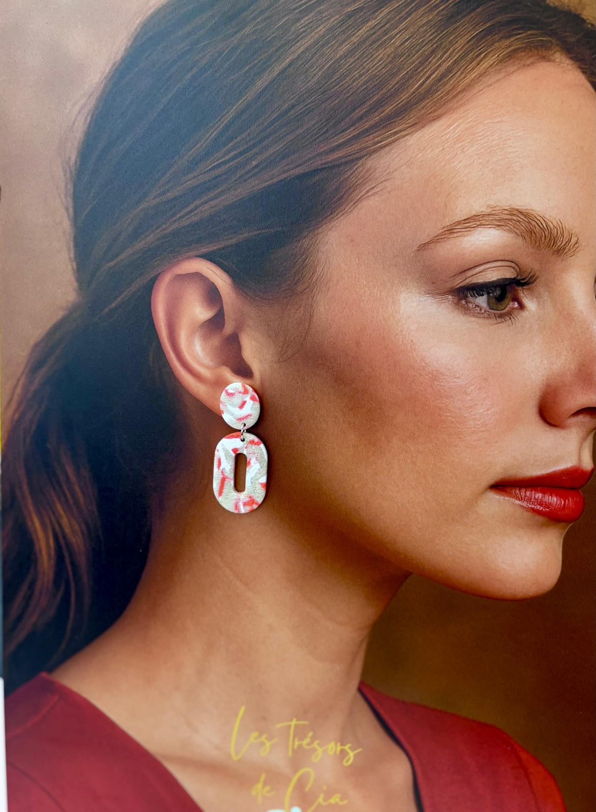 Autre vue des boucles d'oreilles ovales blanc moucheté de rouge corail, la fente centrale traverse le pendant ajouré.