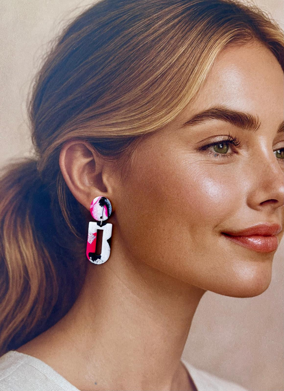 Paire de boucles d'oreilles en arche évidée aux aplats rose fluo, noir et argent, suspendues sous leur puce ronde