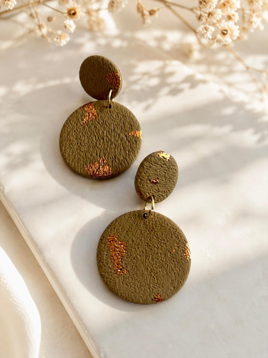 Boucles d'oreilles en argile polymère vert kaki mat, deux disques pleins superposés, un petit sur un grand, avec des éclats de feuille cuivrée dispersés.
