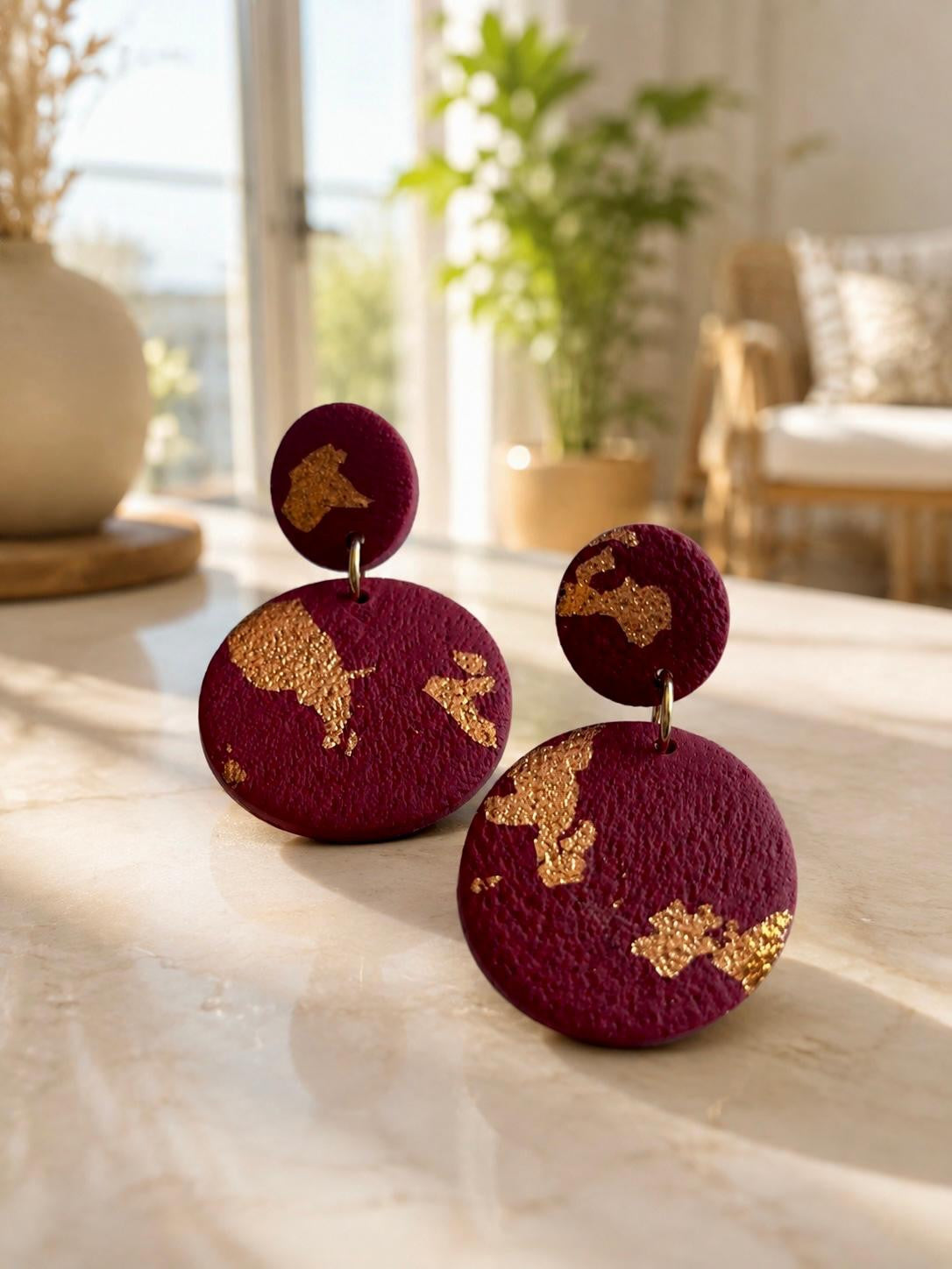 Boucles d'oreilles en argile polymère bordeaux framboise, petit disque posé sur un grand disque pendant, recouverts de larges plaques de feuille dorée.