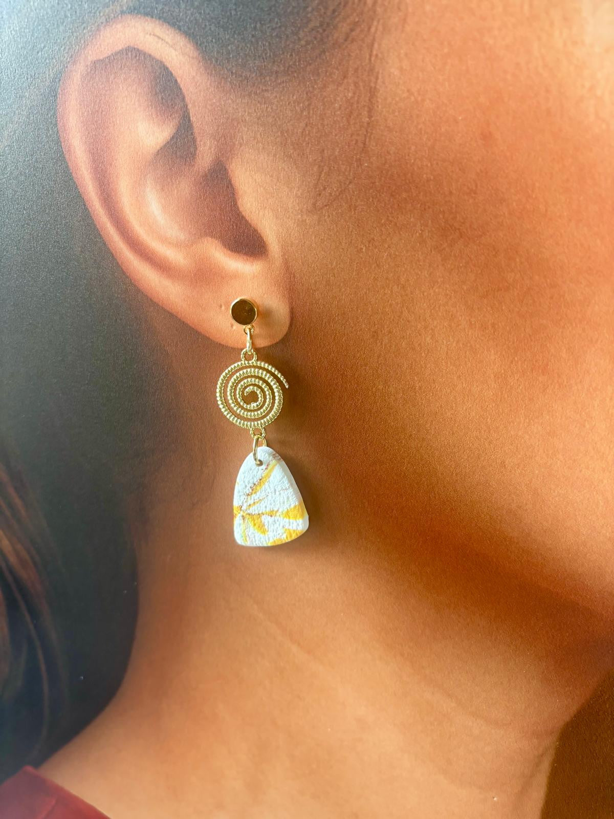 Autre vue des boucles blanc texturé et traits jaune moutarde, la spirale dorée posée au-dessus du pendant triangle aux angles arrondis