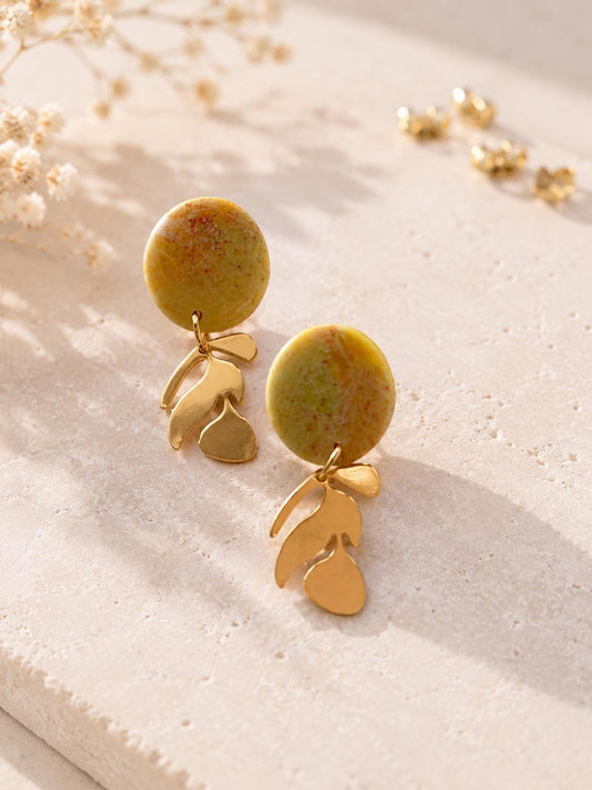 Boucle d'oreille disque en argile vert olive moucheté de rouille, surface mate, et branche dorée à trois feuilles dessous