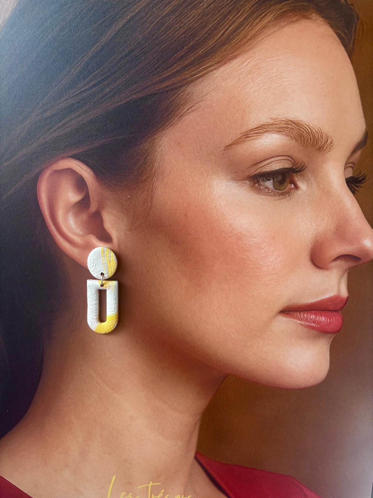 Boucle d'oreille en arche évidée blanche texturée avec une coulée jaune sur le bas, montée sur une puce ronde