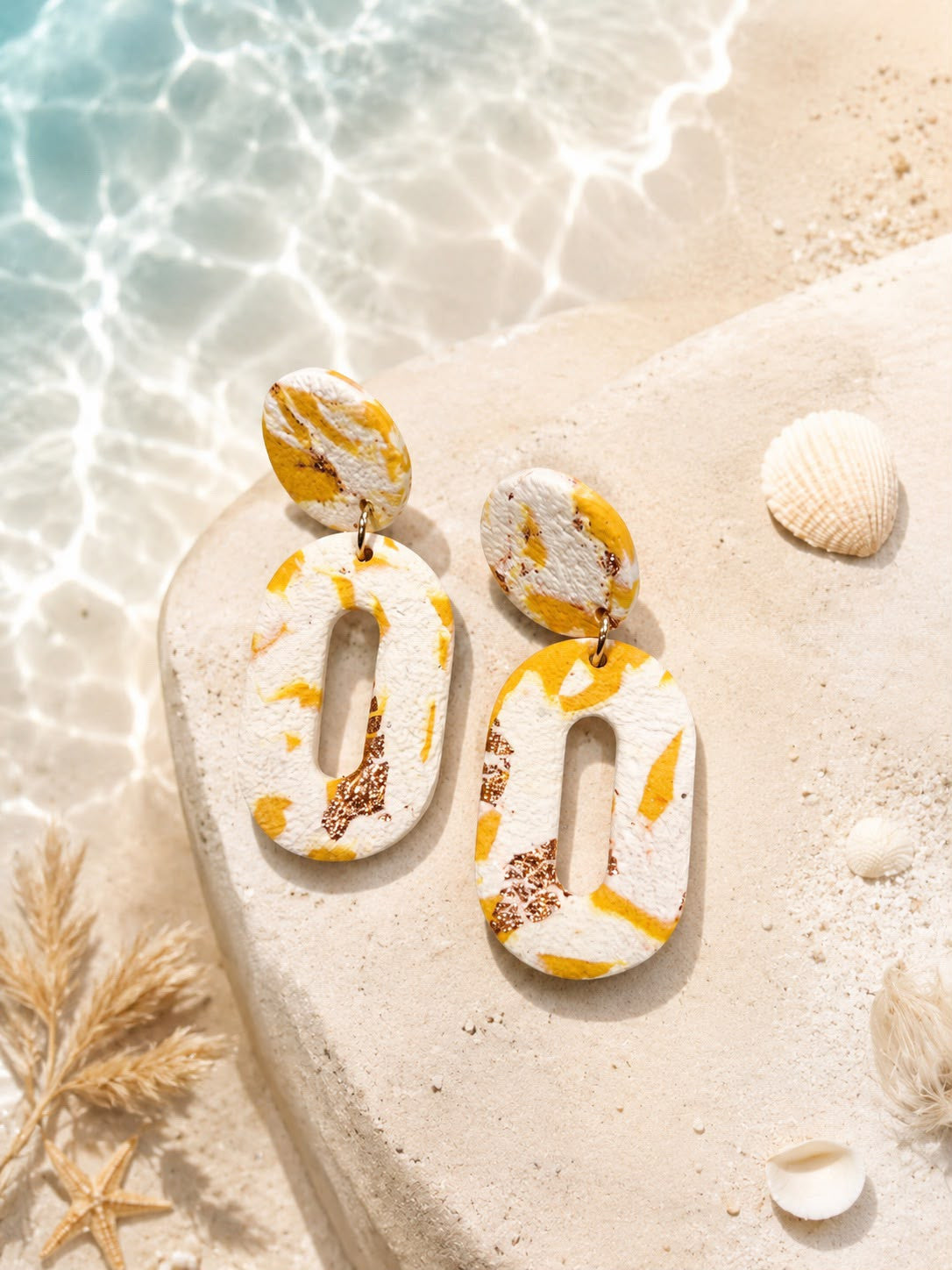 Boucles d'oreilles ovales ajourées en argile blanche et jaune moutarde, avec des paillettes cuivrées agglomérées, puce ronde en haut.