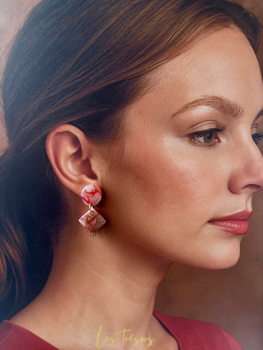 Boucle d'oreille carré marbré rose et rouge avec un cœur doré rayonnant posé dessus, portée
